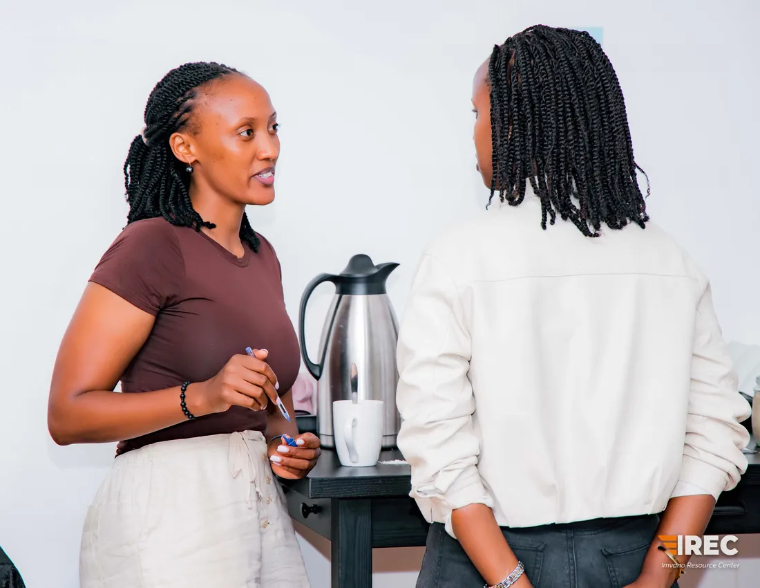 Two participants talking beside a refreshments table with a flask and a cup.