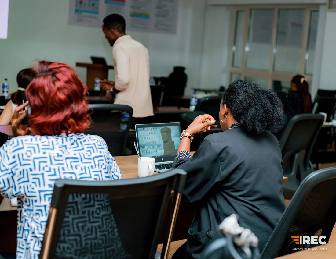 Two participants seen from behind, looking toward the front of the classroom where someone is speaking at a lectern.