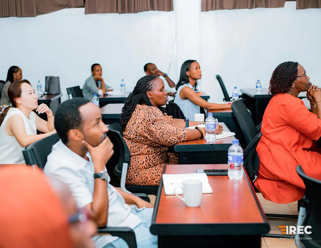 Participants seated in rows at desks and looking toward the front, with notebooks and water bottles on the desks.
