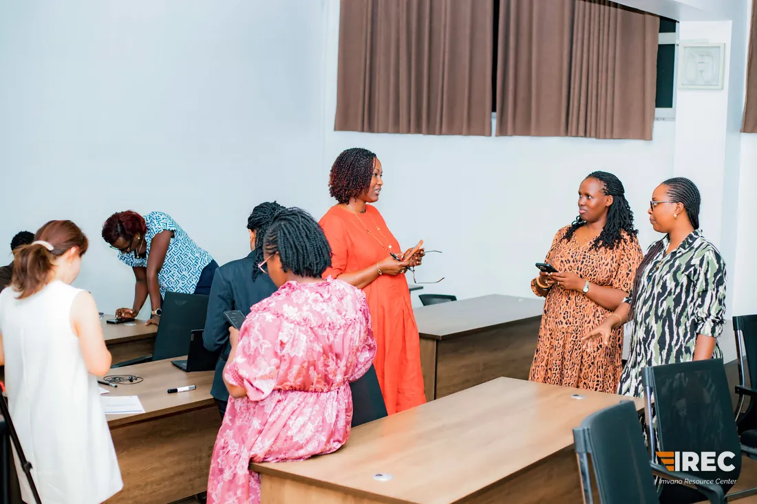 Participants standing and talking in small groups in the classroom, some holding phones, with others at laptops behind.